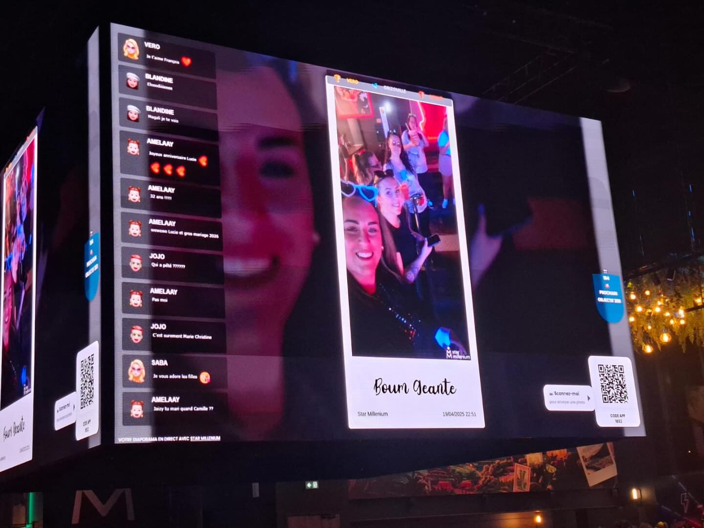 Giant indoor screen showing a festive group photo, live comments and QR codes under red and blue lighting
