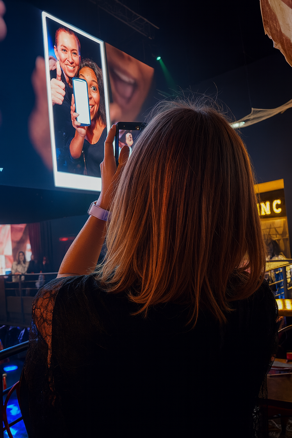 Person seen from behind photographing a giant vertical screen showing two smiling people in a dark multimedia installation