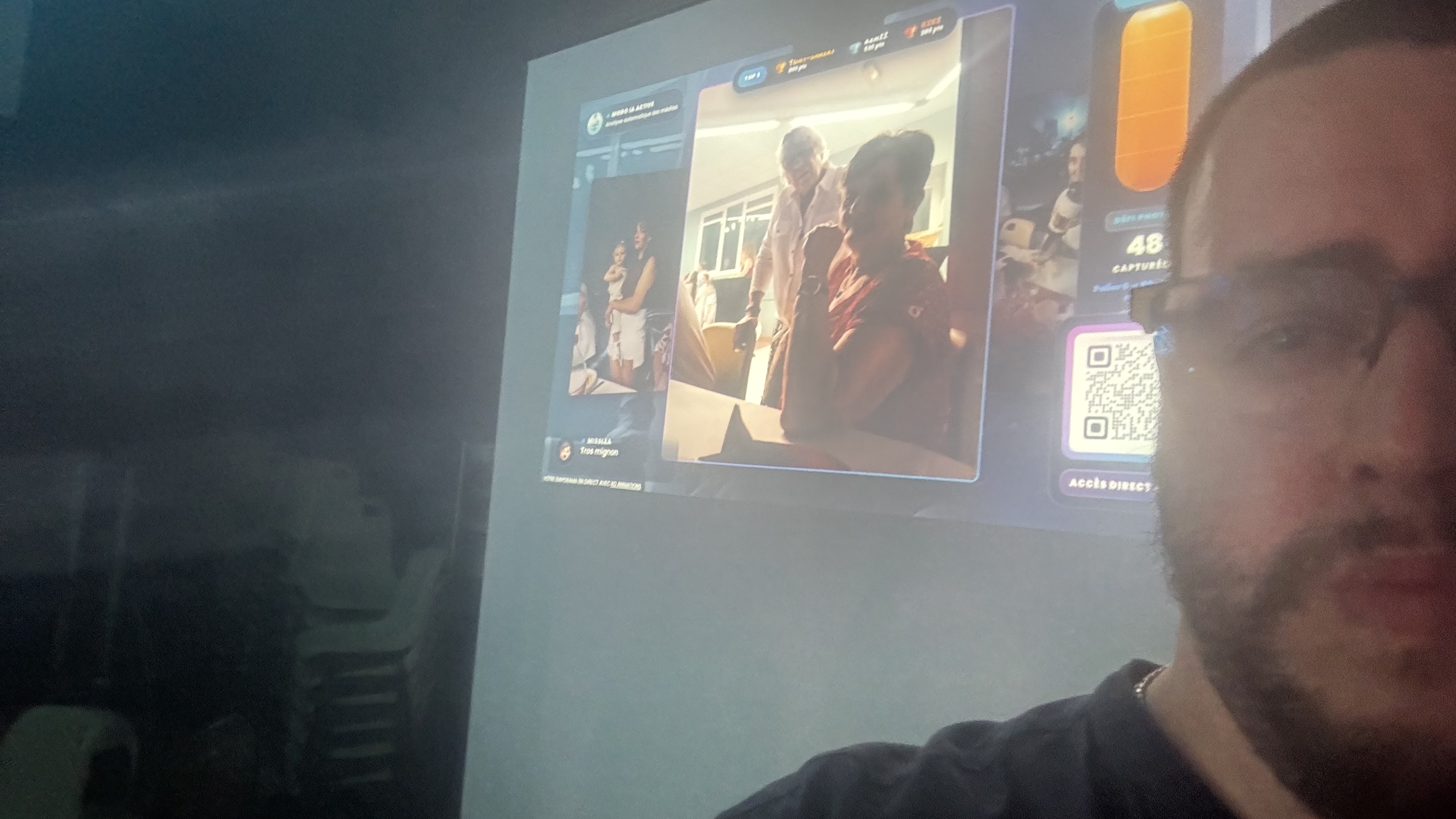 Een persoon maakt een selfie terwijl een familiefoto en een PhotoSharing-QR-code op een groot scherm worden geprojecteerd.