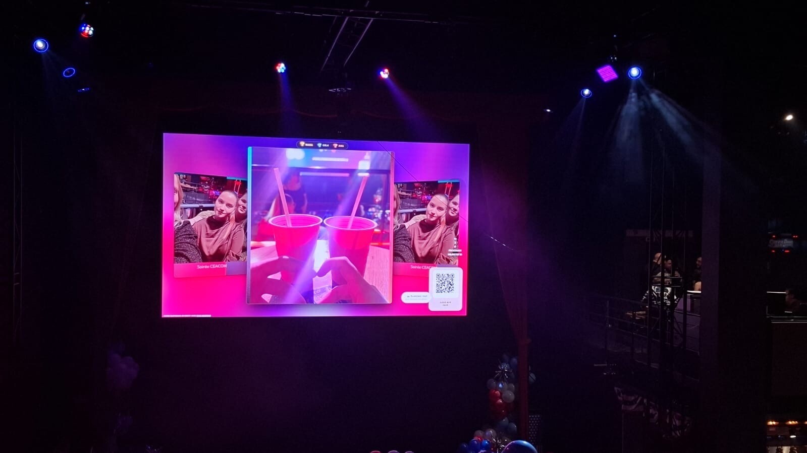 Grand écran rose diffusant une photo de deux gobelets rouges avec un QR code dans une salle sombre